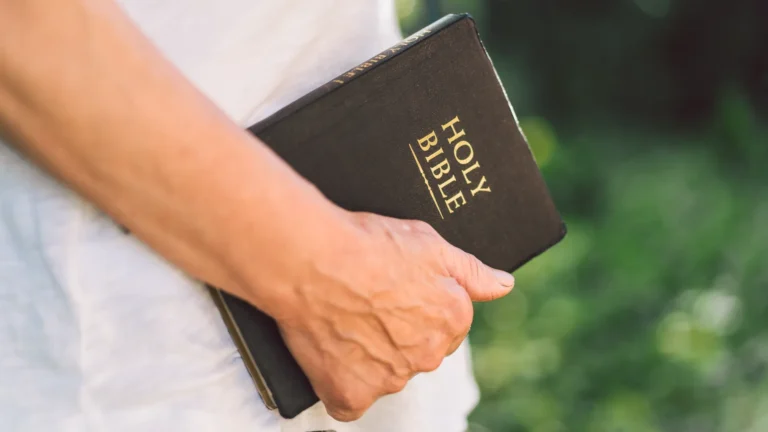 A person holds a black Holy Bible, a blueprint for a healthy life, with a blurred green background. Advent Hill Ministries